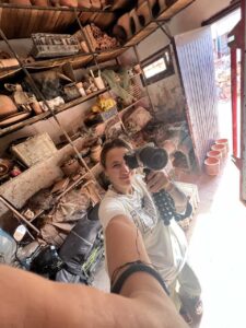Rebecca in a selfie in a workshop warehouse with a camera in her hand.